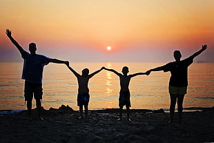 silhouette of man, woman with their two boys holding while raising their hands in front of beach during sunset