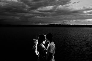 couple kissing near body of water grayscale photography