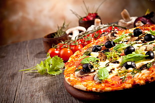 shallow focus photography of pizza topped with basil, olives, and tomatoes
