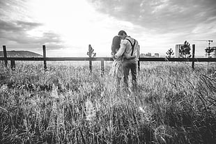 couple on grass field beside wooden fence hugging