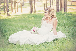 woman in white sweetheart bridal gown sitting on grass during daytime