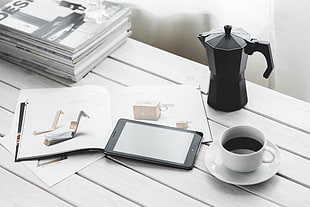 white ceramic tea cup beside black iPad and pitcher on table