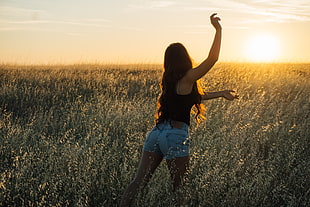 woman wearing black top and blue shorts standing on grasses during sunset \
