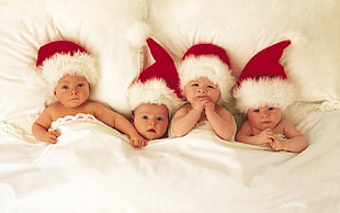 four babies wearing red Santa hats lying on bed HD wallpaper