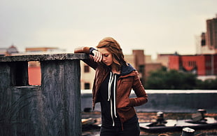 woman in brown leather zip-up hoodie leaning on grey wall during daytime