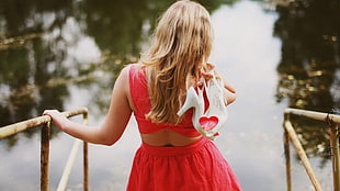 woman wearing red crop top and skirt holding white heeled shoes near water