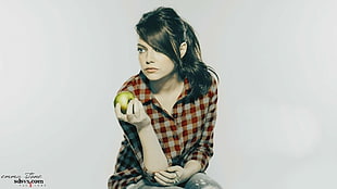 woman wears red and white checkered long-sleeved shirt holds apple fruit