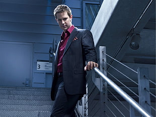 men's black suit jacket holding gray handrails