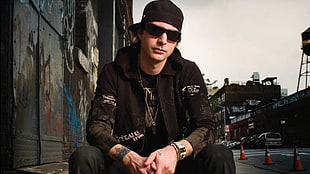 man in black jacket, sunglasses, and cap near graffiti wall