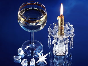 closeup photo of lighted candle on clear glass holder beside empty cup