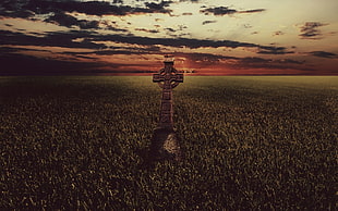 landscape photography of green field with cross statue during golden hour