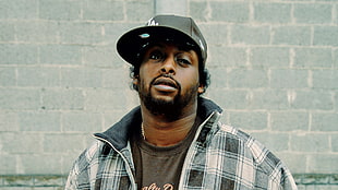 man wearing black fitted cap and white-and-grey plaid zip-up jacket HD wallpaper