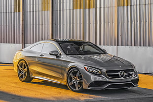 gray Mercedes-Benz coupe parked on gray pavement near gray steel wall