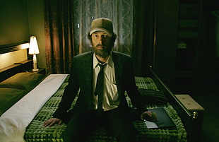 man in black suit sitting on mattress inside room