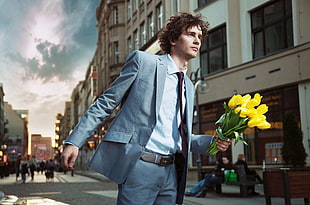 man in grey notched lapel suit jacket while holding bouquet of yellow tulips
