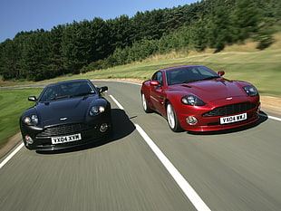 two red and black Aston Martin cars speeding on road at dayti,e