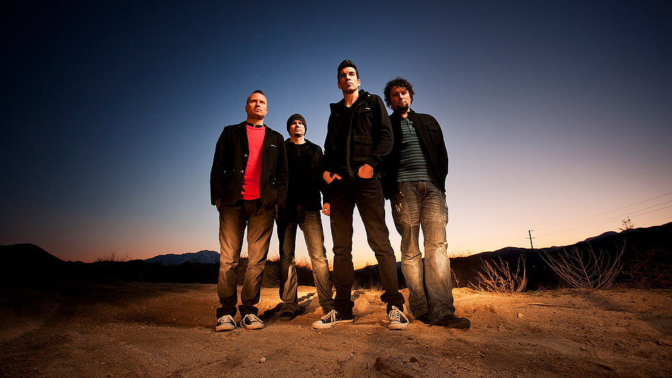 four men standing on brown soil ground near mountains HD wallpaper