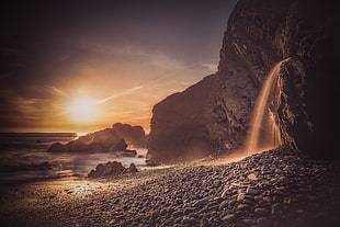 waterfalls on rocky mountain near seashore during sunset