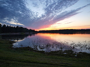 lake surrounded by trees under cloudy sky during sunset