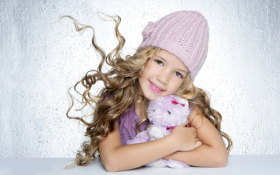 toddler girl wearing purple knit hat and purple top holding plush toy HD wallpaper