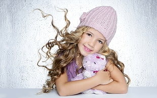 toddler girl wearing purple knit hat and purple top holding plush toy