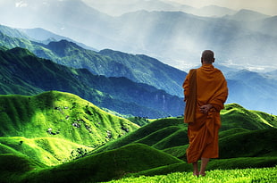 monk standing on green mountain during daytime