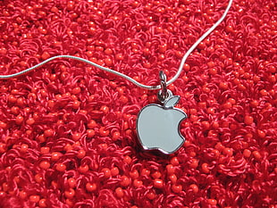 silver Apple pendant necklace on top of red textile