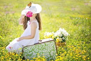 girl in white dress sitting on suitcase on green grass field