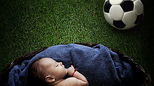 baby lying on blue textile near soccer ball