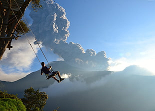 man sitting on the swing near erupting volcano