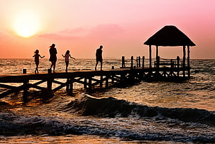 silhouette of family walking on dock beside waving sea