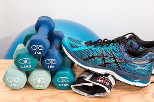 six fixed weight dumbbells and blue ASICS running shoes on brown table
