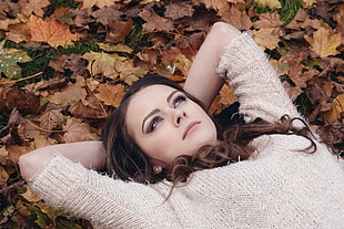 woman in beige knit shirt lying on ground with brown leaves