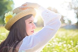 woman wearing white long-sleeved shirt holding brown sunhat with yellow flower