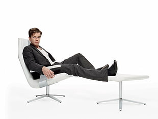 man wearing black formal suit sitting on glider chair