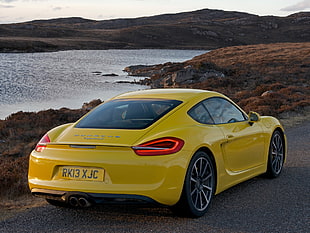 yellow Porsche sports car on asphalt road near body of water