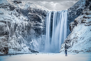 person standing front of skogafoss in iceland HD wallpaper