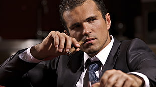 man in black formal suit jacket holding brown cigar