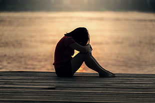 woman in purple shirt sitting on dock near body of water during sunset