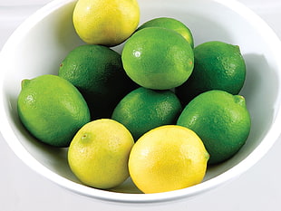 green and yellow lemons on white ceramic bowl