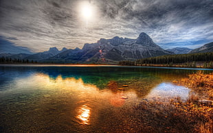 mountain near river under grey clouds at daytime