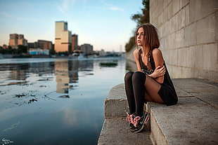 woman wearing black top sitting on concrete stair near body of water under cloudy sky at daytime HD wallpaper