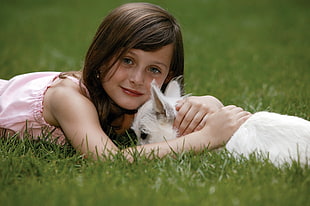 girl in pink dress laying down on green grasses hugging white Chihuahua
