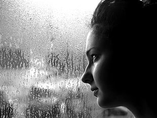 greyscale photography of woman facing glass window