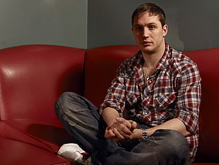 man in red and blue flannel shirt sitting on red leather couch