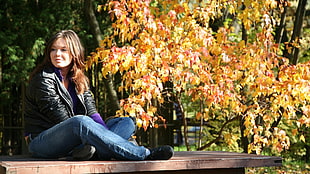 woman in black leather jacket sitting on wooden platform