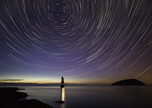 black and white lighthouse near body of water under star timelapse