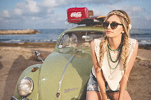 woman in white crew-neck sleeveless top sitting on green Volkswagen Beetle at during daytime