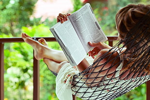 woman in white strapless dress on hammock reading book