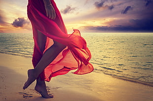 woman in red dress walking in front of beach
